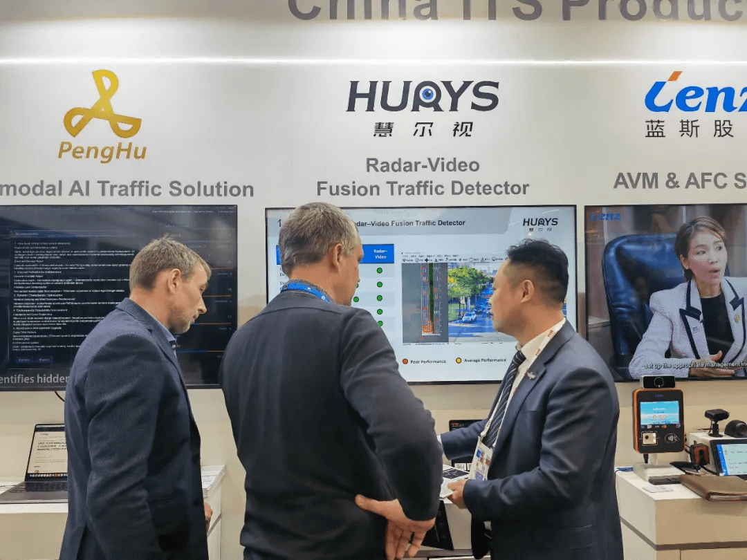 Three men reviewing a 'HUAYS Radar-Video Fusion Traffic Detector' display at a trade show.